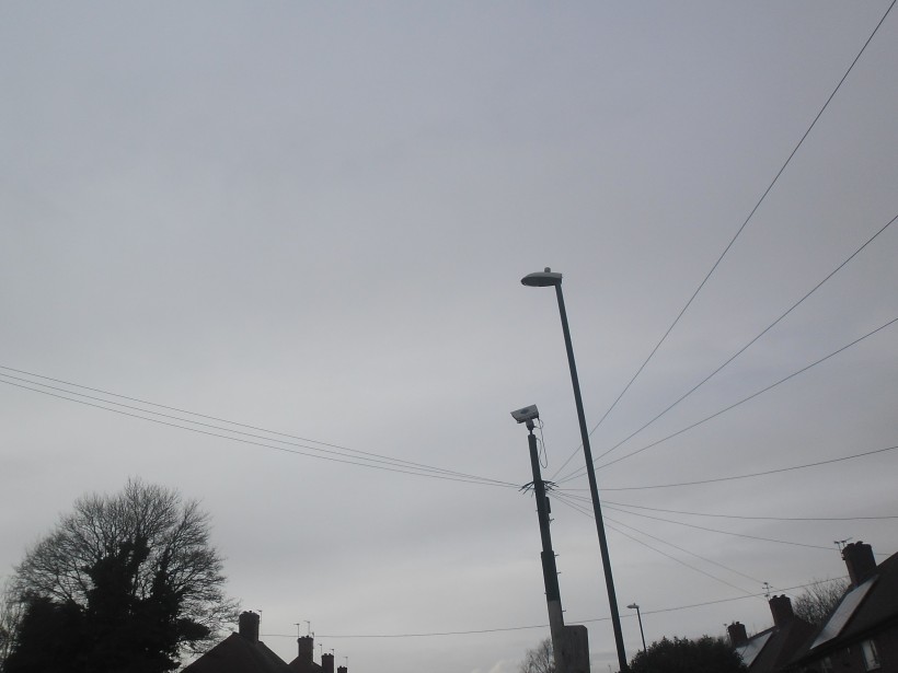rooftops, a lamp-post and CCTV pole against the grey sky, photo taken from my front garden at home